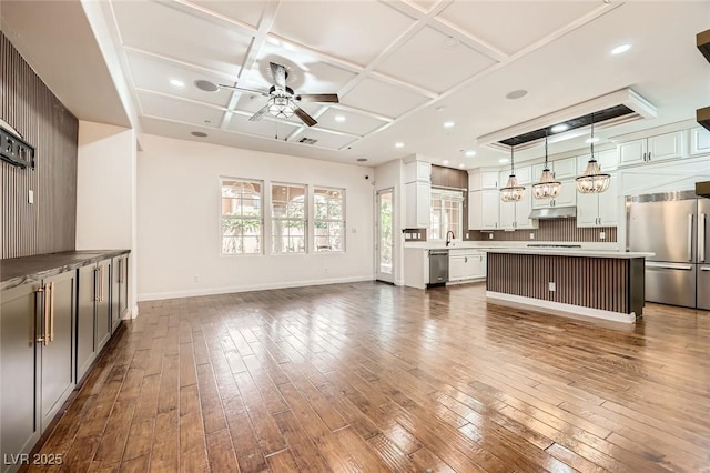 unfurnished living room featuring a sink, coffered ceiling, baseboards, ceiling fan, and dark wood-style floors