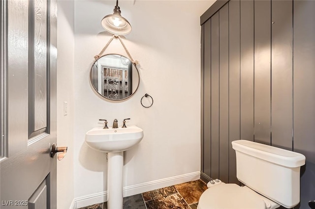bathroom with toilet, baseboards, and stone finish floor