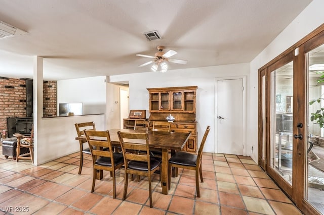 dining room with a wood stove, light tile patterned flooring, ceiling fan, and visible vents
