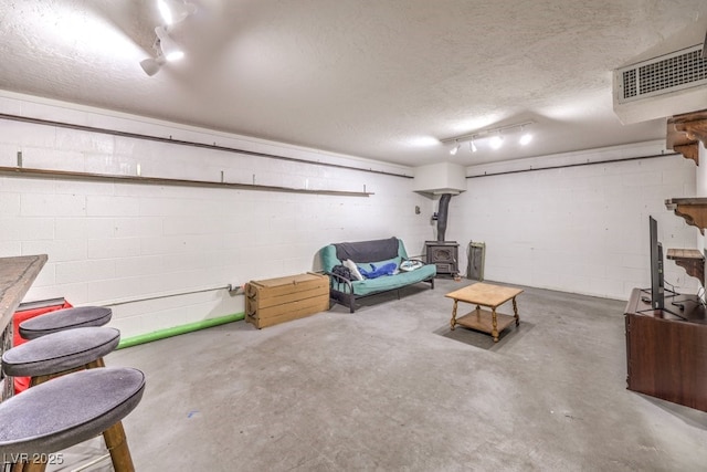 unfurnished living room with a textured ceiling, unfinished concrete flooring, visible vents, a wood stove, and concrete block wall