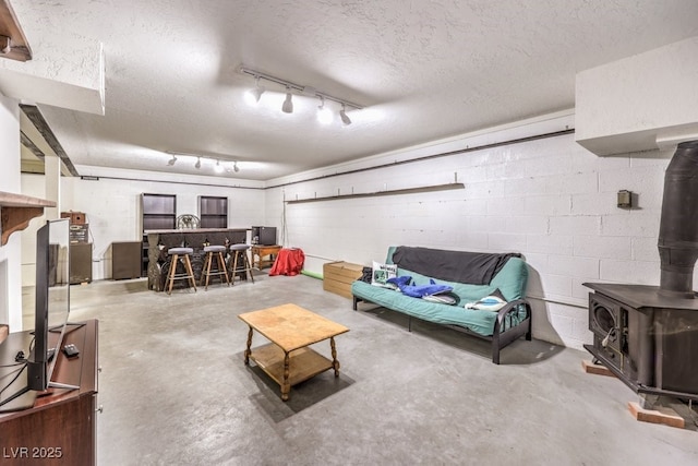 living room with a textured ceiling, a wood stove, rail lighting, and concrete flooring