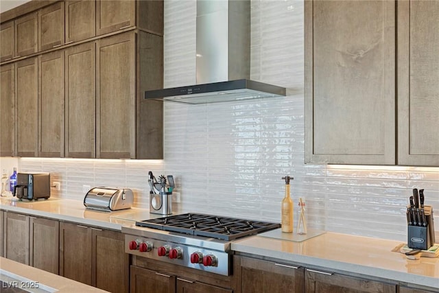 kitchen with stainless steel gas stovetop, a toaster, wall chimney exhaust hood, backsplash, and light countertops