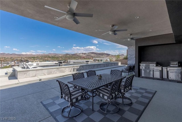 view of patio featuring a mountain view, exterior kitchen, outdoor dining space, ceiling fan, and grilling area