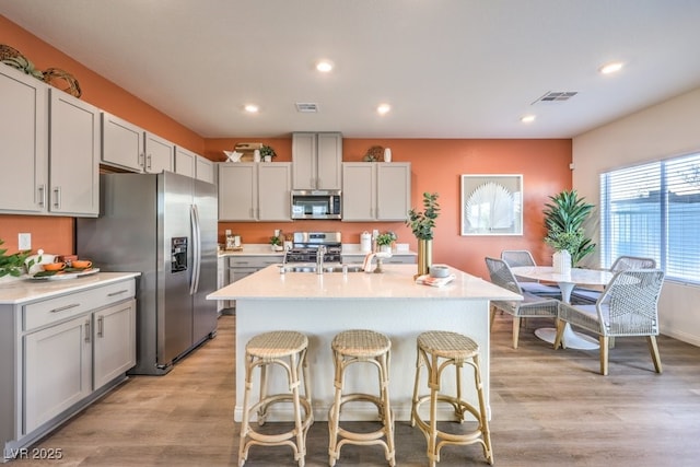 kitchen featuring stainless steel appliances, a kitchen breakfast bar, light wood-type flooring, visible vents, and light countertops