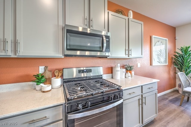 kitchen with light stone counters, stainless steel appliances, gray cabinets, and light wood-style floors