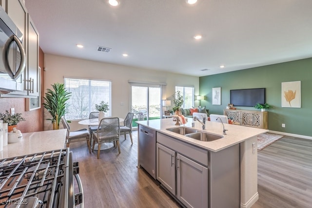 kitchen with a sink, open floor plan, wood finished floors, appliances with stainless steel finishes, and gray cabinets