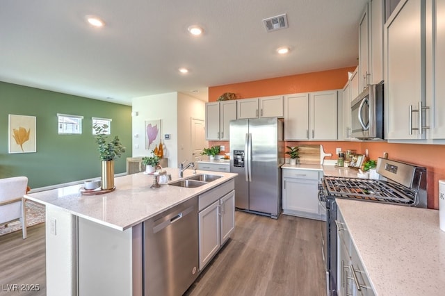 kitchen with a sink, appliances with stainless steel finishes, a center island with sink, visible vents, and light wood-style floors