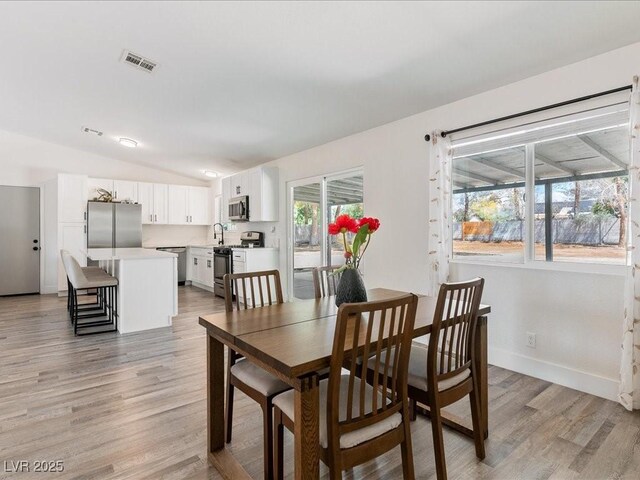 dining room with light wood-style flooring, lofted ceiling, and baseboards