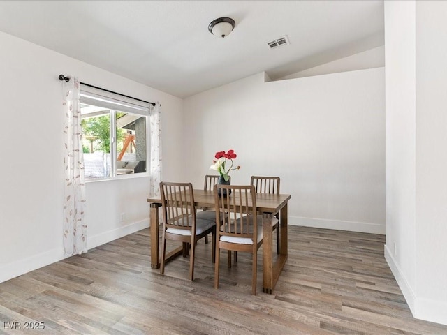dining room featuring light wood-style floors, vaulted ceiling, and baseboards