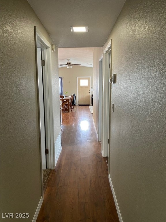 hallway featuring baseboards, a textured wall, and wood finished floors