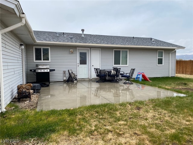 back of property with a lawn, a patio, a shingled roof, and fence