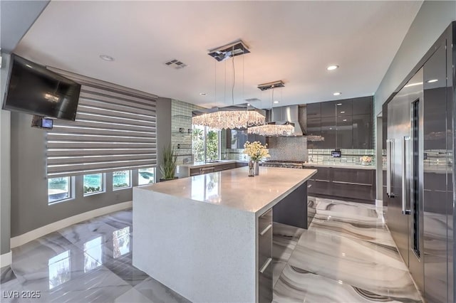 kitchen with wall chimney range hood, modern cabinets, marble finish floor, and stainless steel built in refrigerator