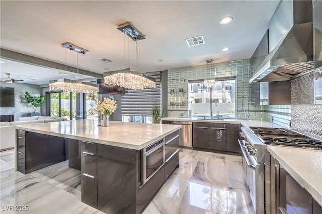 kitchen featuring wall chimney range hood, light countertops, appliances with stainless steel finishes, and modern cabinets