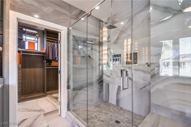 bathroom featuring a marble finish shower, marble finish floor, a healthy amount of sunlight, and a walk in closet