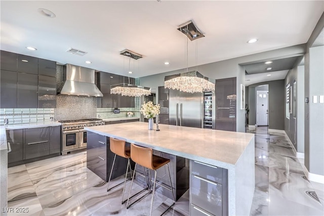 kitchen with marble finish floor, premium appliances, modern cabinets, a chandelier, and wall chimney exhaust hood