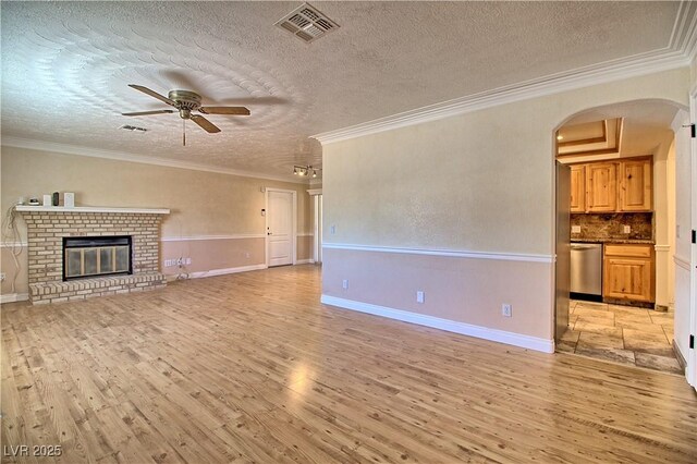unfurnished living room featuring light wood finished floors, ceiling fan, a textured ceiling, arched walkways, and ornamental molding
