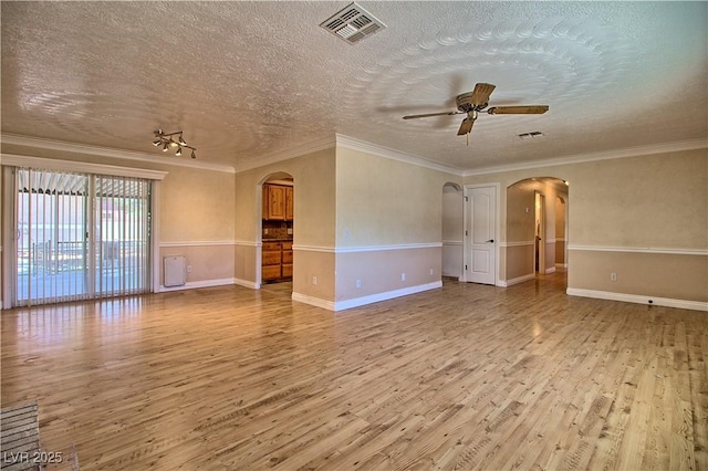 empty room with arched walkways, wood finished floors, a textured ceiling, a ceiling fan, and crown molding