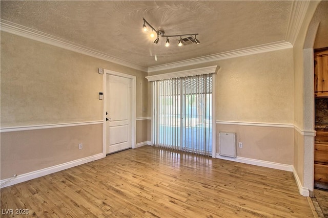 empty room with wood finished floors, ornamental molding, a textured ceiling, baseboards, and track lighting