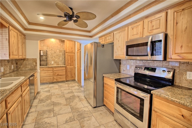 kitchen featuring stainless steel appliances, a raised ceiling, light brown cabinets, tasteful backsplash, and a sink
