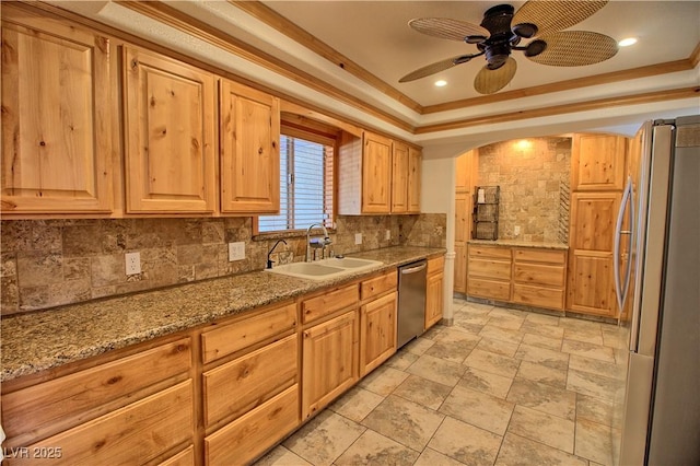 kitchen featuring stainless steel appliances, a sink, decorative backsplash, a raised ceiling, and a ceiling fan