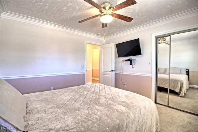 bedroom featuring a closet, a textured ceiling, carpet flooring, ornamental molding, and a ceiling fan