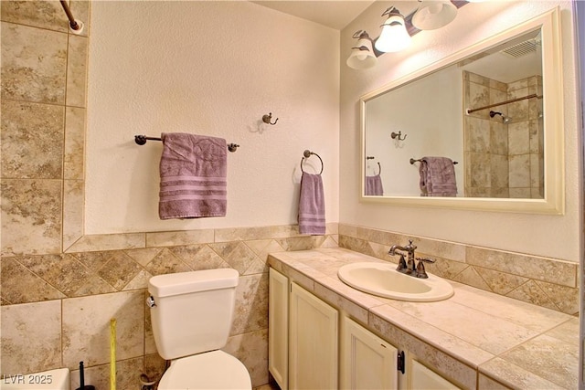 bathroom with toilet, vanity, a shower, and tile walls