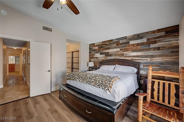 bedroom with an accent wall, lofted ceiling, wooden walls, a closet, and baseboards