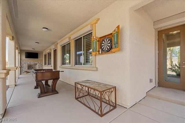 recreation room featuring a textured ceiling, an outdoor stone fireplace, and a textured wall