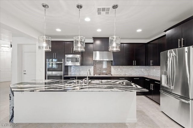 kitchen with appliances with stainless steel finishes, under cabinet range hood, backsplash, recessed lighting, and a kitchen island with sink