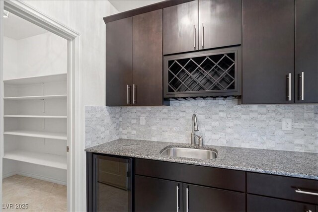 kitchen featuring a sink, beverage cooler, light stone counters, dark brown cabinetry, and backsplash