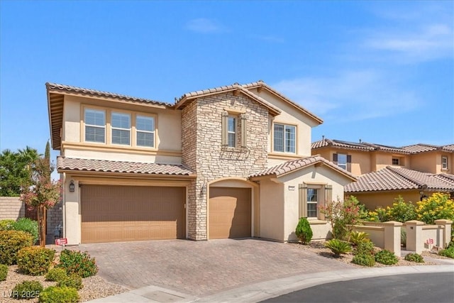 mediterranean / spanish-style house featuring stone siding, stucco siding, a tiled roof, and a garage