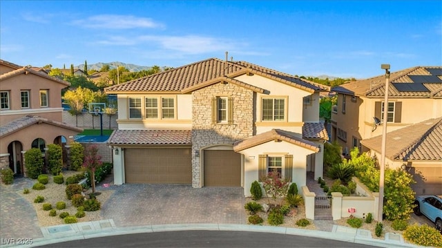 mediterranean / spanish-style home featuring a tiled roof, stucco siding, a garage, stone siding, and decorative driveway