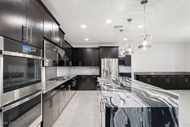 kitchen with stainless steel appliances, tasteful backsplash, a sink, pendant lighting, and light stone counters