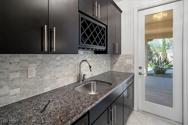 kitchen with a sink, dark cabinetry, tasteful backsplash, and dark stone countertops