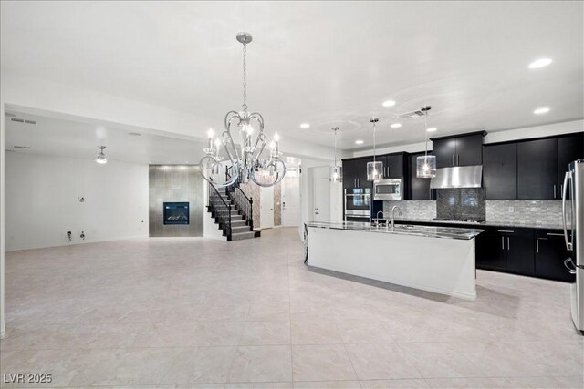 kitchen with appliances with stainless steel finishes, dark cabinetry, under cabinet range hood, a large fireplace, and recessed lighting