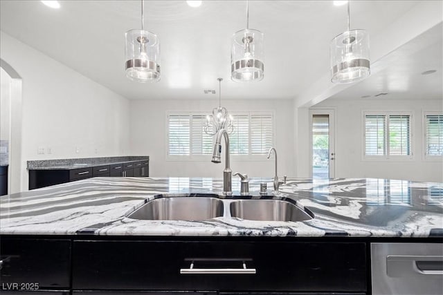 kitchen with a sink, pendant lighting, arched walkways, dishwasher, and light stone counters
