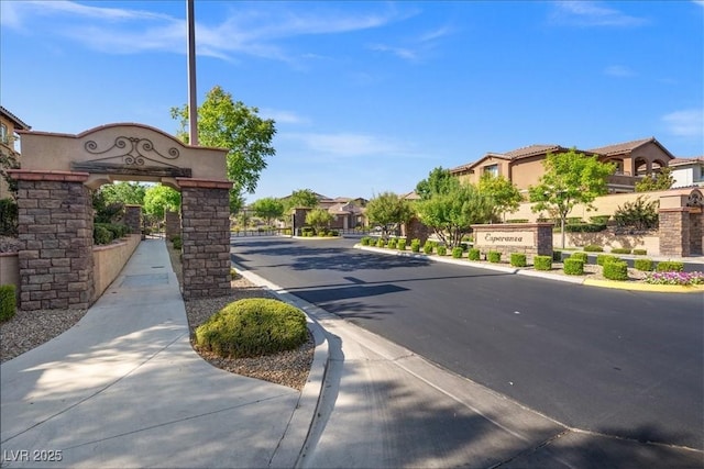 view of road featuring a gated entry, a residential view, curbs, and sidewalks