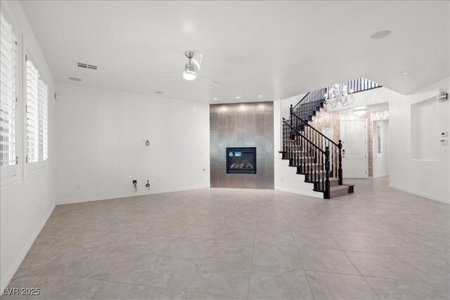 unfurnished living room with stairs, a tiled fireplace, a chandelier, baseboards, and a ceiling fan