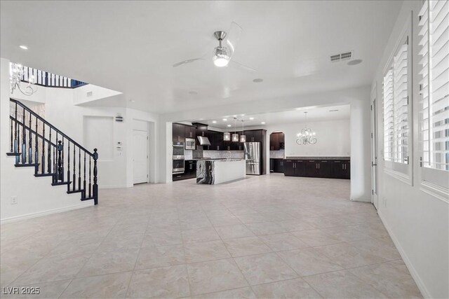 unfurnished living room featuring a chandelier, a ceiling fan, light tile patterned flooring, and baseboards