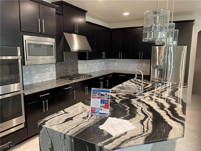 kitchen featuring under cabinet range hood, appliances with stainless steel finishes, a sink, light stone countertops, and a center island with sink