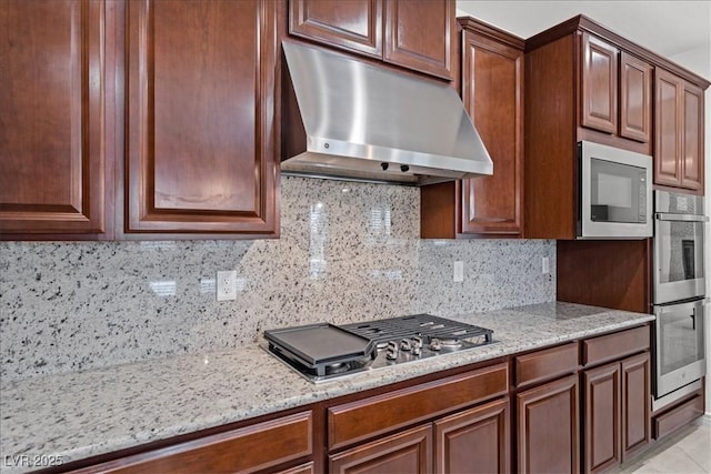 kitchen featuring under cabinet range hood, stainless steel appliances, tasteful backsplash, and light stone counters