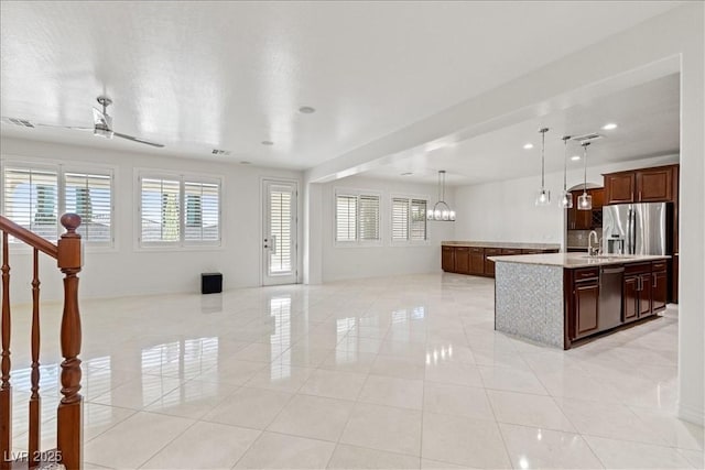 kitchen with an island with sink, a sink, pendant lighting, open floor plan, and light countertops