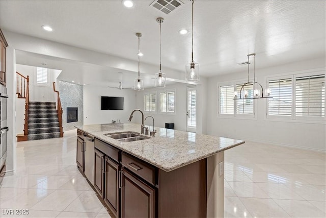 kitchen with baseboards, visible vents, a sink, open floor plan, and a center island with sink