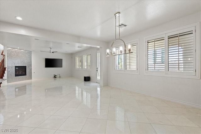 interior space featuring visible vents, baseboards, a fireplace, and ceiling fan with notable chandelier