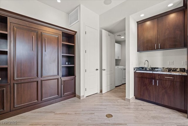 kitchen featuring light wood finished floors, a sink, open shelves, separate washer and dryer, and dark brown cabinetry
