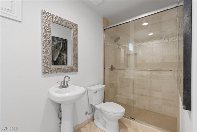 bathroom with a stall shower, toilet, a sink, and baseboards