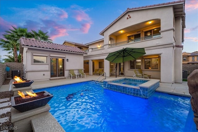 back of house at dusk with an outdoor fire pit, a balcony, a patio area, and stucco siding