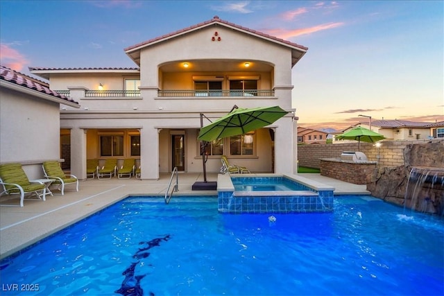 rear view of property featuring a balcony, a patio, stucco siding, and a pool with connected hot tub