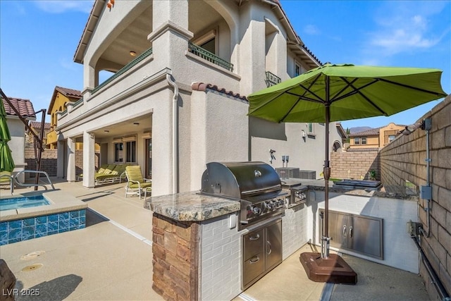 view of patio / terrace featuring a balcony, an outdoor kitchen, area for grilling, an in ground hot tub, and a fenced backyard