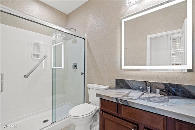 full bath featuring vanity, toilet, a textured wall, and a shower stall